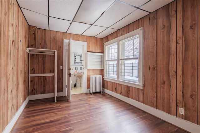 unfurnished bedroom featuring radiator heating unit, wood finished floors, baseboards, and wood walls