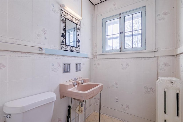 bathroom with tile walls, toilet, radiator heating unit, and a sink