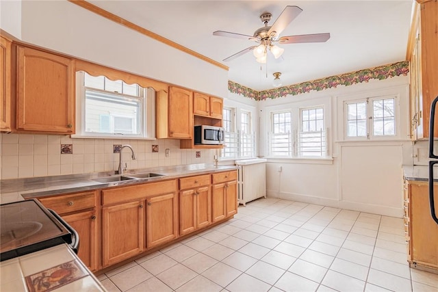 kitchen featuring stainless steel microwave, backsplash, ceiling fan, stainless steel counters, and a sink