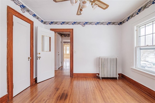 spare room featuring a wealth of natural light, ceiling fan, radiator heating unit, and light wood-style floors