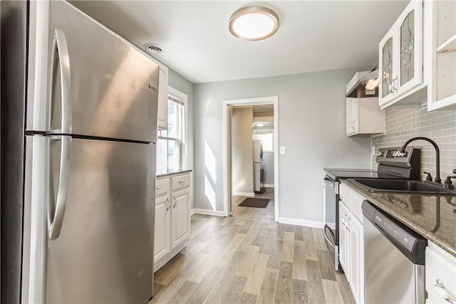 kitchen featuring light wood finished floors, backsplash, appliances with stainless steel finishes, white cabinets, and a sink