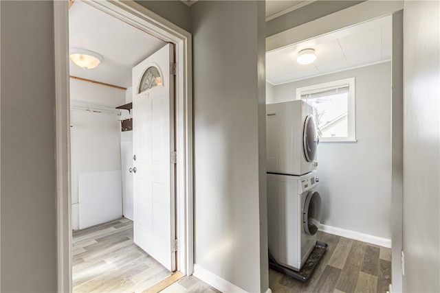 laundry area featuring laundry area, stacked washing maching and dryer, baseboards, and wood finished floors