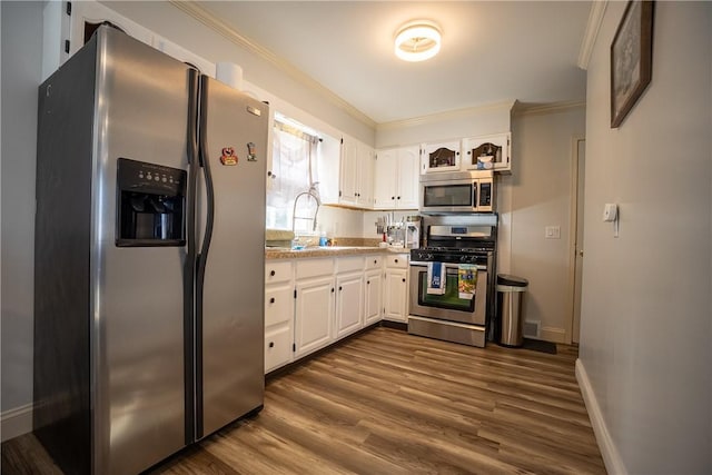 kitchen with dark wood-style floors, stainless steel appliances, light countertops, white cabinetry, and crown molding