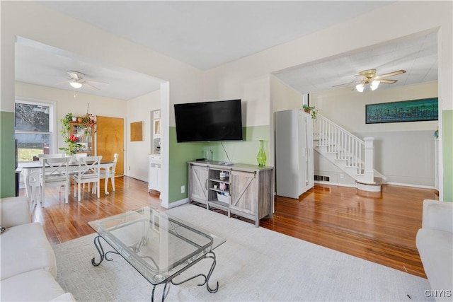 living room featuring stairs, wood finished floors, baseboards, and ceiling fan