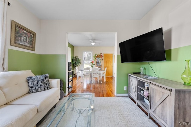 living area with light wood finished floors, a ceiling fan, and baseboards