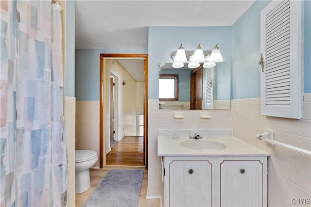 full bathroom featuring vanity, tile walls, toilet, and a wainscoted wall