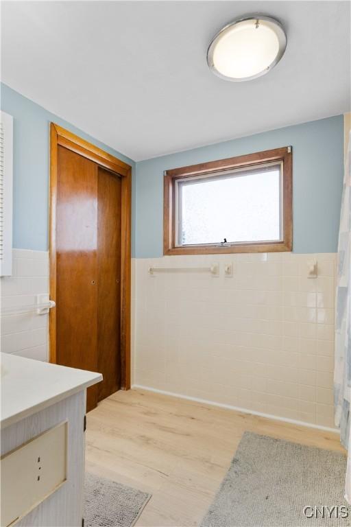 interior space featuring a wainscoted wall, tile walls, vanity, and wood finished floors