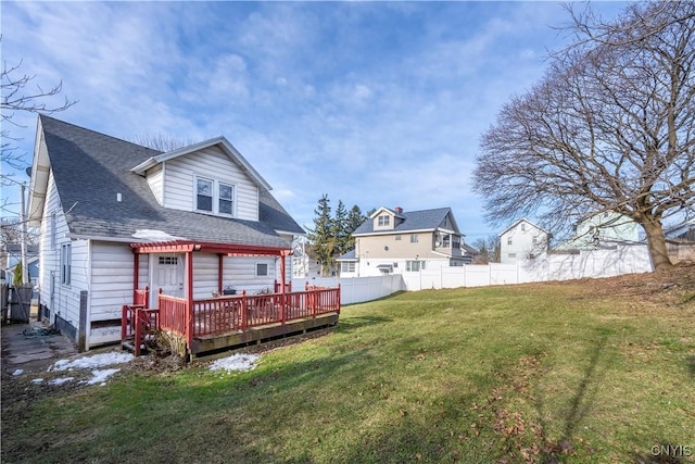 back of house with a lawn, a shingled roof, a deck, and fence