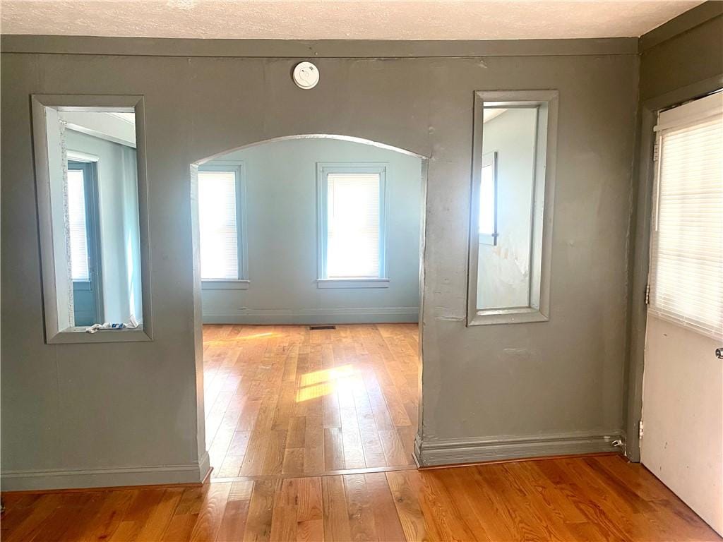 spare room with baseboards, arched walkways, and light wood-style flooring