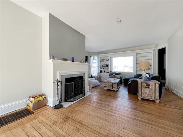 living room featuring a fireplace with flush hearth, baseboards, and light wood-type flooring