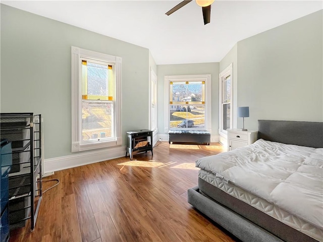 bedroom featuring ceiling fan, baseboards, wood finished floors, and a wood stove