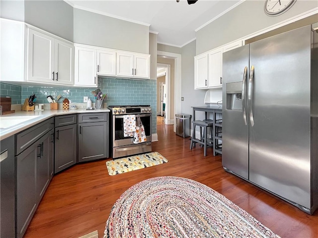 kitchen with ornamental molding, tasteful backsplash, wood finished floors, white cabinetry, and appliances with stainless steel finishes