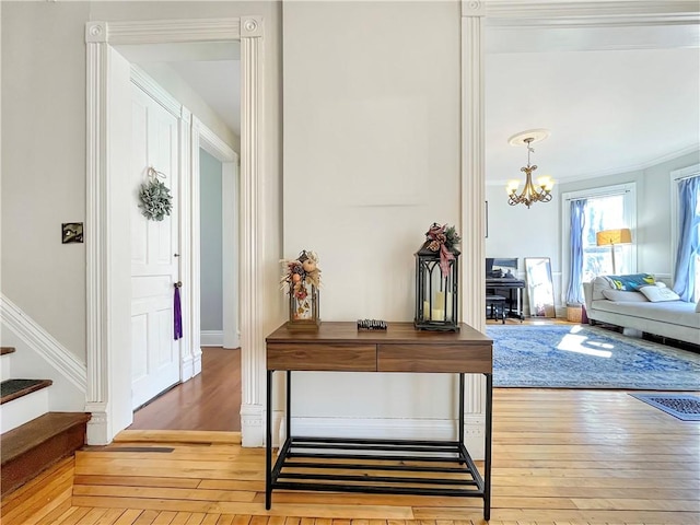 interior space featuring baseboards, light wood-type flooring, stairs, ornamental molding, and a notable chandelier