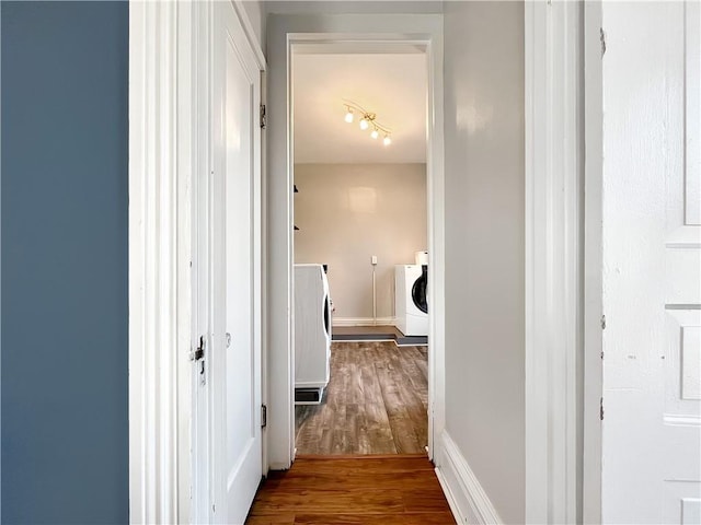 hall featuring independent washer and dryer, baseboards, and wood finished floors