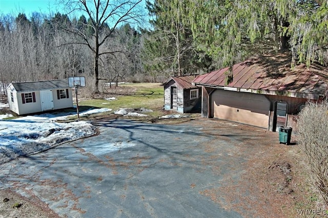 exterior space featuring a forest view, aphalt driveway, a yard, and an outdoor structure