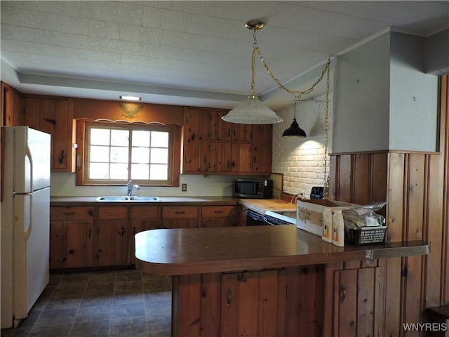 kitchen featuring stainless steel microwave, brown cabinets, a peninsula, freestanding refrigerator, and a sink