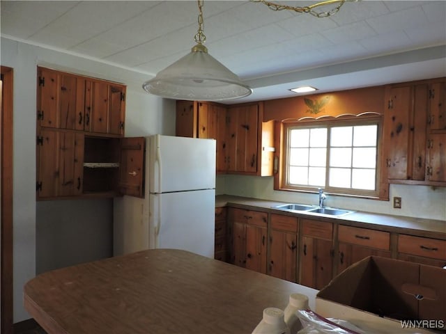 kitchen featuring hanging light fixtures, brown cabinetry, freestanding refrigerator, and a sink