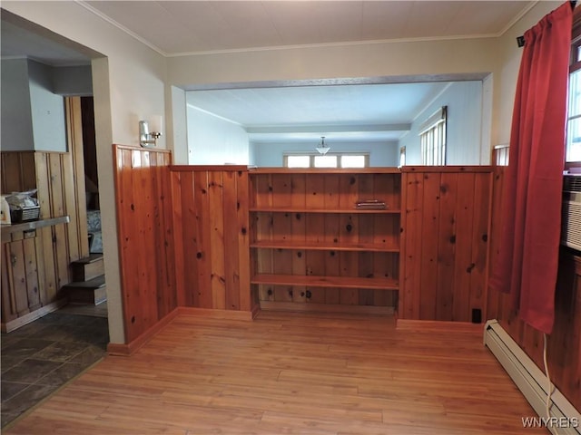 interior space featuring wooden walls, baseboard heating, wood finished floors, and crown molding