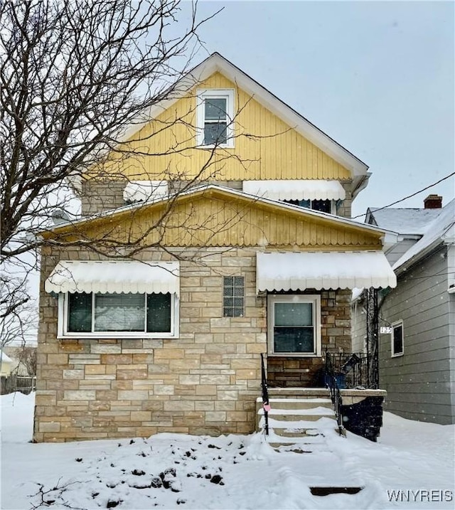 snow covered property with stone siding