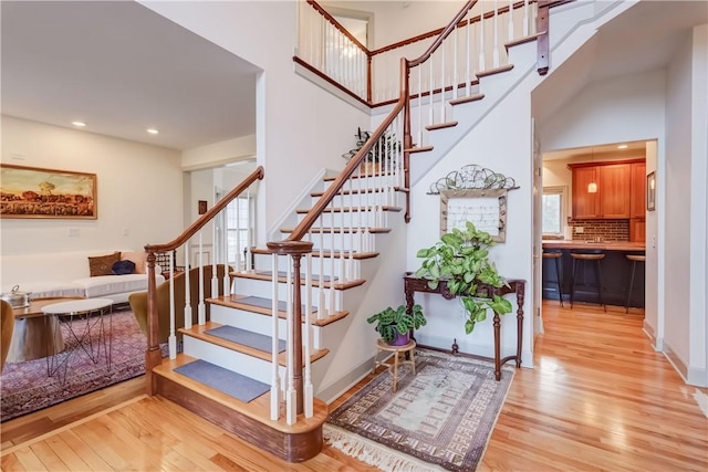 staircase featuring recessed lighting, baseboards, a towering ceiling, and wood finished floors