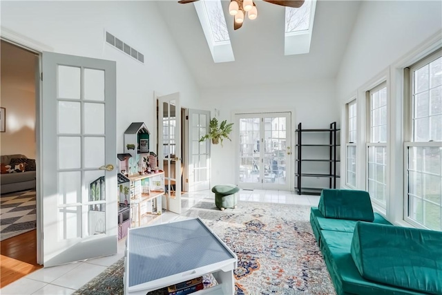 tiled living area with visible vents, high vaulted ceiling, a skylight, and a ceiling fan