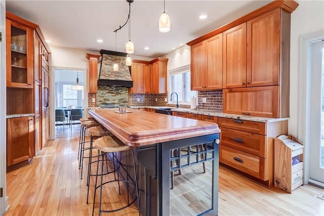 kitchen featuring custom exhaust hood, light wood-type flooring, backsplash, and butcher block counters