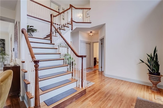 staircase with baseboards, a towering ceiling, and hardwood / wood-style floors