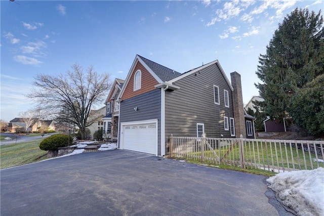 view of side of property featuring aphalt driveway, fence, and a chimney