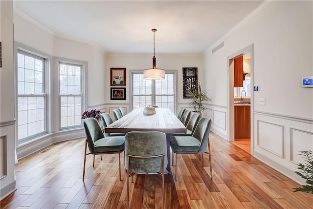 dining area featuring a decorative wall, light wood-style floors, visible vents, and wainscoting