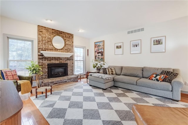 living room featuring a brick fireplace, light wood-style floors, visible vents, and a wealth of natural light