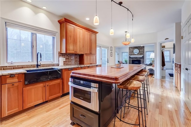 kitchen featuring light stone counters, light wood-type flooring, backsplash, and a brick fireplace