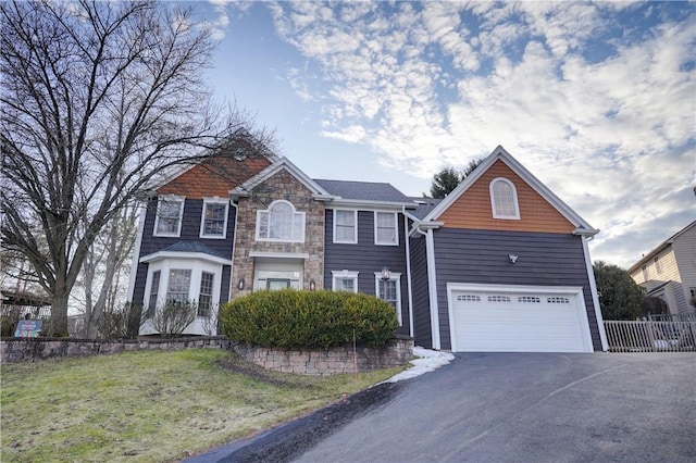 view of front facade with a front lawn, fence, stone siding, and aphalt driveway