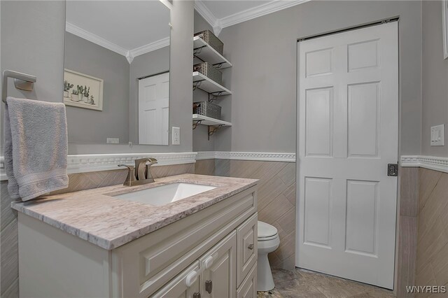 half bathroom featuring a wainscoted wall, toilet, ornamental molding, tile walls, and vanity