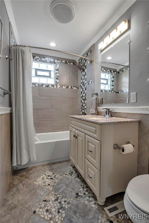 bathroom featuring tile walls, toilet, shower / bath combo, and visible vents