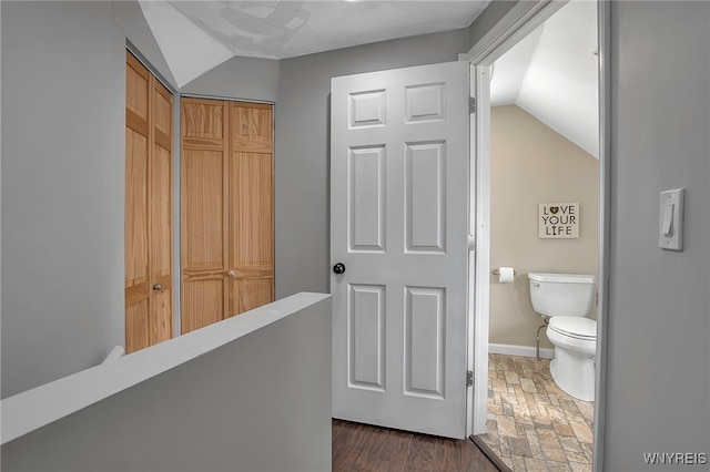 bathroom featuring toilet, stone finish flooring, baseboards, and vaulted ceiling