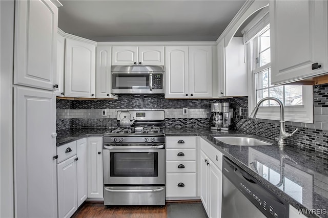 kitchen with dark stone counters, decorative backsplash, white cabinets, stainless steel appliances, and a sink