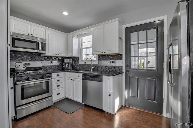 kitchen with a sink, decorative backsplash, white cabinets, stainless steel appliances, and dark wood-style flooring