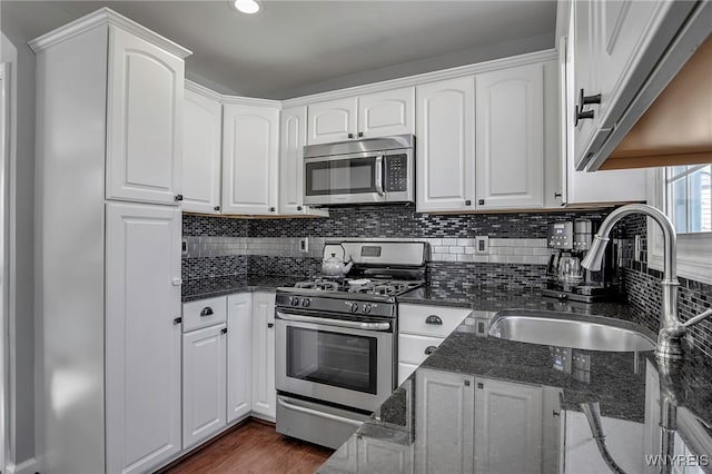 kitchen featuring dark stone counters, a sink, stainless steel appliances, white cabinets, and backsplash