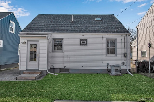 back of property with central air condition unit, a shingled roof, a yard, and fence