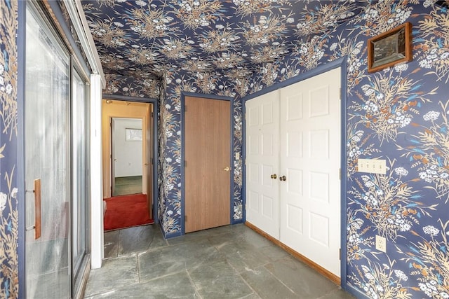 unfurnished bedroom featuring stone finish floor, wallpapered walls, and baseboards