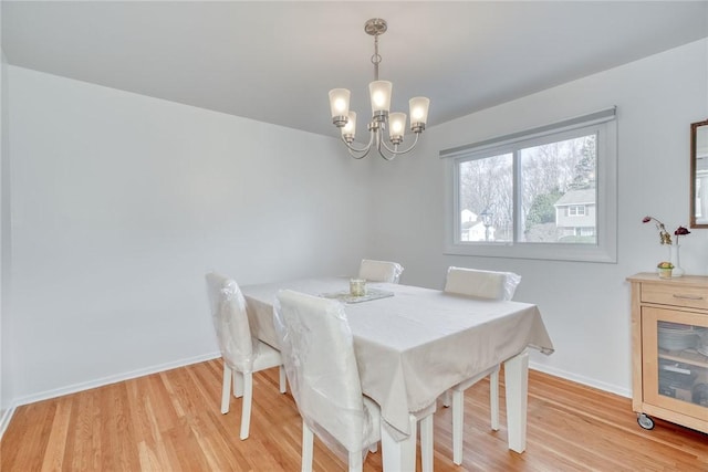 dining area with light wood-type flooring, baseboards, and a notable chandelier