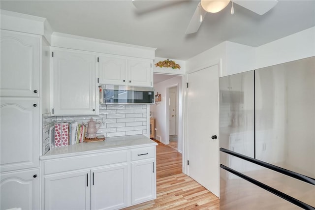 kitchen with light wood finished floors, stainless steel microwave, tasteful backsplash, light countertops, and white cabinets