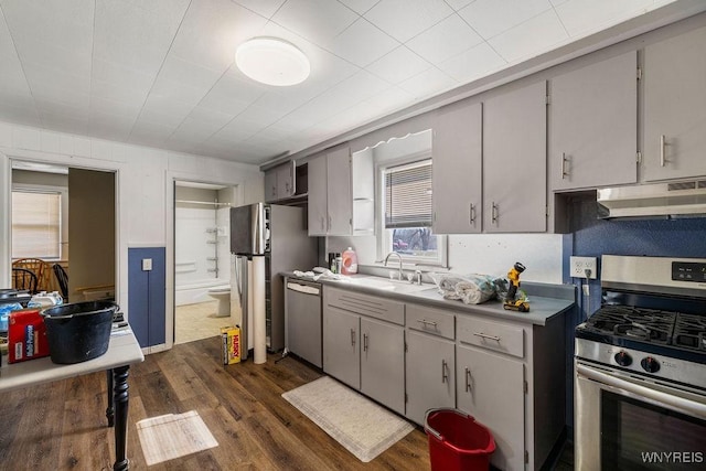 kitchen featuring dark wood-style flooring, a sink, gray cabinetry, stainless steel appliances, and under cabinet range hood