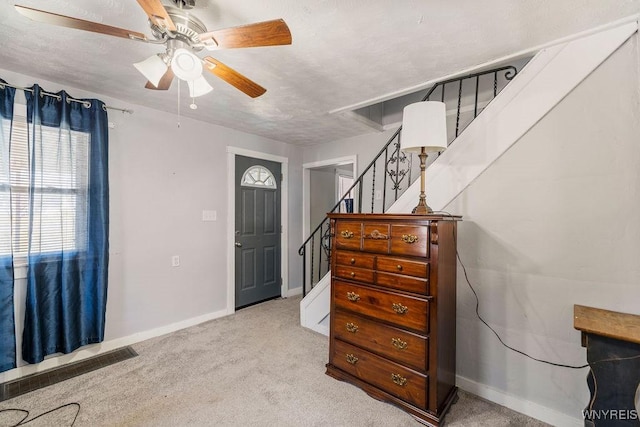 entrance foyer featuring baseboards, stairway, light colored carpet, a textured ceiling, and a ceiling fan