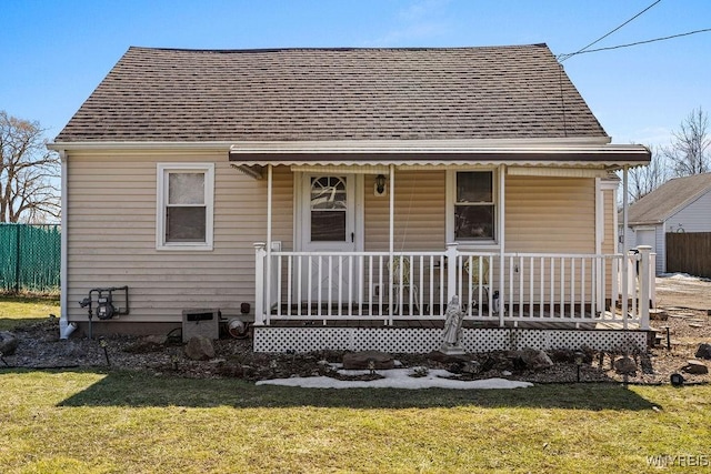 view of front of house featuring a front yard, fence, covered porch, and a shingled roof