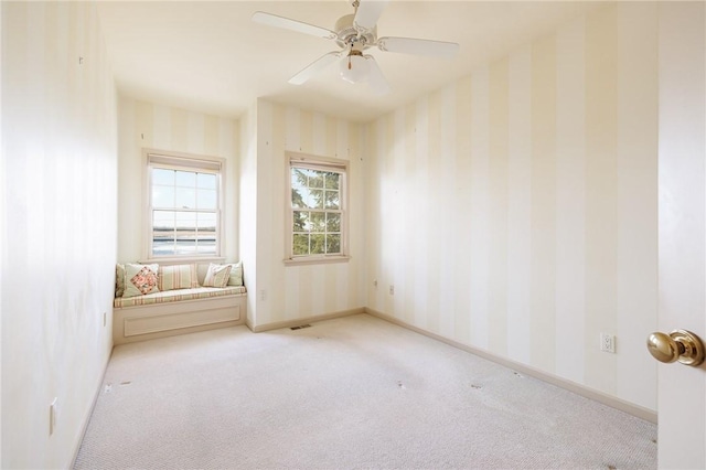 carpeted empty room with visible vents, wallpapered walls, baseboards, and a ceiling fan