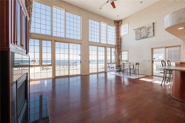 living area featuring a towering ceiling, a fireplace, dark wood-style floors, and a ceiling fan