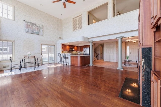 unfurnished living room with wood-type flooring, a high ceiling, ceiling fan, and ornate columns