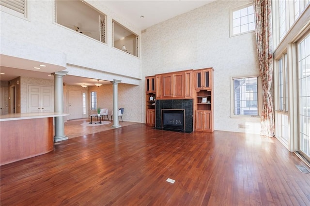 unfurnished living room featuring visible vents, dark wood-type flooring, a fireplace, a high ceiling, and ornate columns