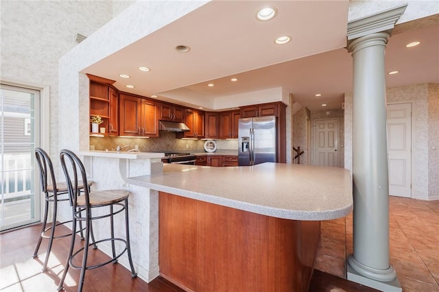 kitchen featuring under cabinet range hood, open shelves, appliances with stainless steel finishes, a peninsula, and brown cabinetry